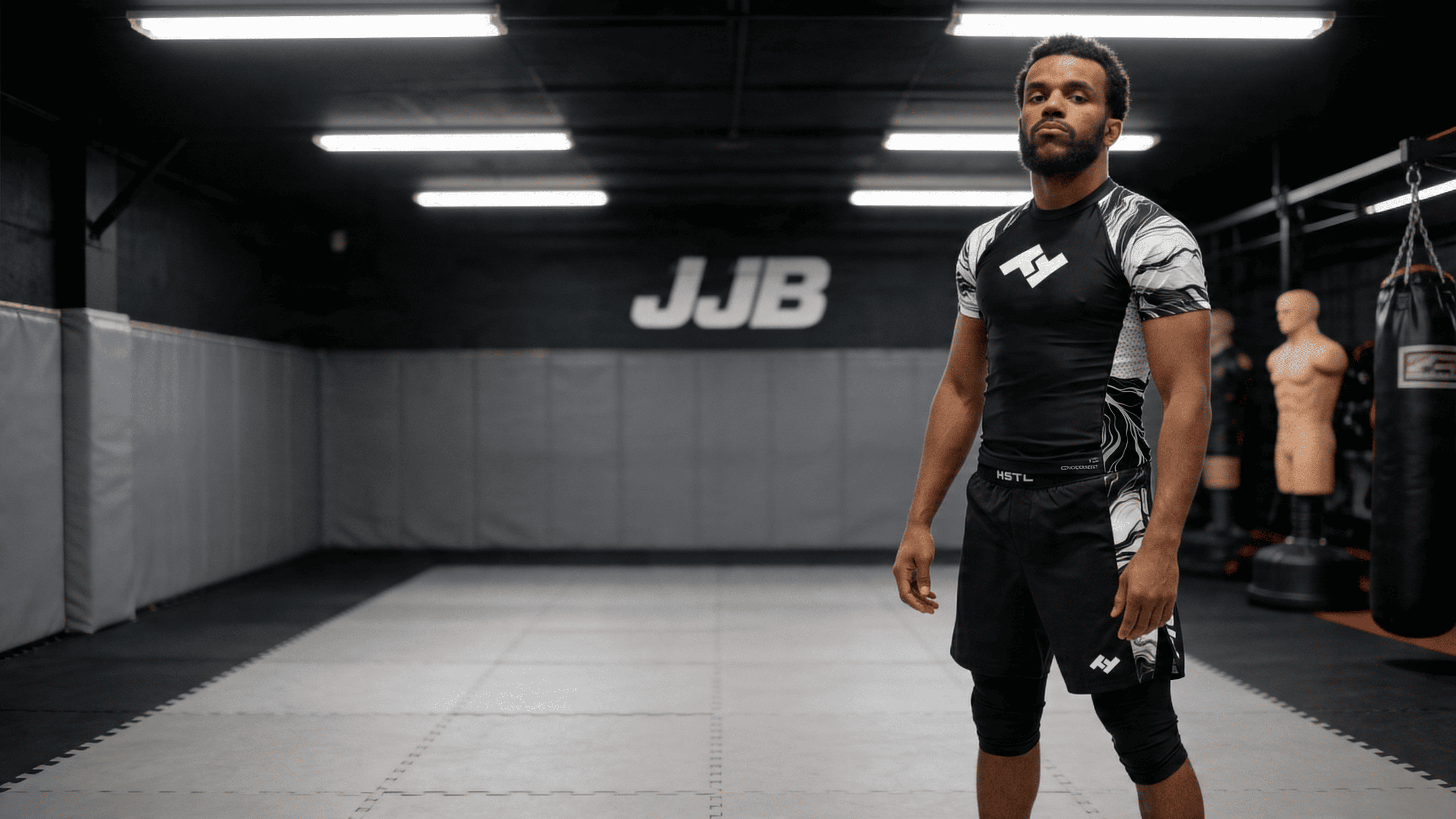 Homme portant un t-shirt de compression/rashguard dans une salle de jjb Hustle Fightwear ajusté dans une salle de JJB avec tatamis gris